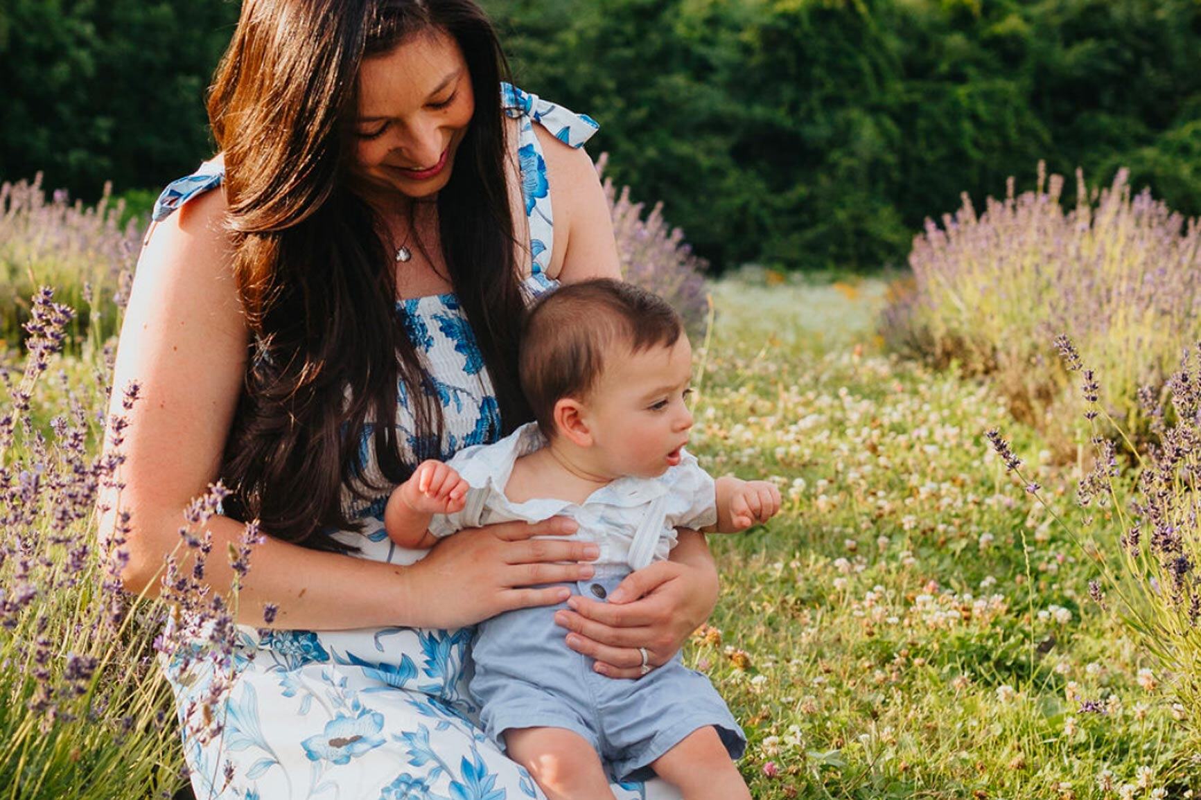 A soft image of Amy, a new mom, kneeling down holding her newborn baby boy. 